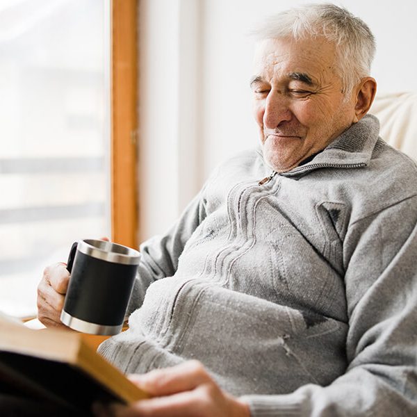 Senior man old sitting and Reading a book at the retirement nursing home with cup of tea in hand